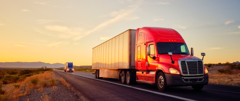 Red semi-trailer truck travelling followed by a blue semi-trailer truck
